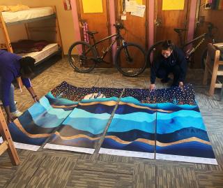 (L-R) Boxelder Dormitory 4 Manager Mikaela Laney and student Lanique Red Tomahawk lay out a cheerful mural for installation on the day room wall. Photo by Josh Gade.