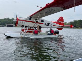 A seaplane floating on the water. The seaplane is white with red markings on the tip of nose, wings and tail.