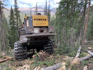 A picture of a piece of heavy equipment working on a hillside that heavily forested.