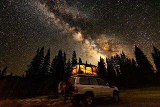 A nighttime picture of a vehicle with a roof-top-tent and with night skies with very vibrant, visible stars.