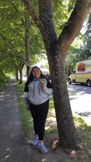 A picture of a student standing near an urban tree, growing between a city street and a sidewalk.