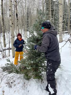 Nelson Rodas, lightly dusted with snow, poses on one side of small tree. His son, Jahir, smiles from the other side.