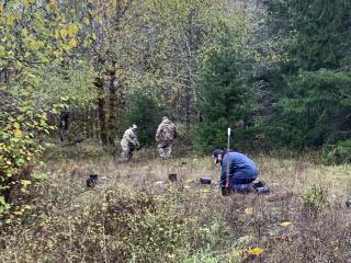 Volunteers with plants in containers. These native plants are being planted in forest. Three volunteers are visible working to plant the containers.