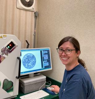 Kayla Herriman sitting at a seed xray maching with her right hand on the computer mouse, and looking back at the camera over her left shoulder.