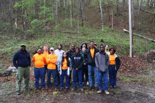 A group of individual (15 in total) stand together, posing for a group photo. On the left side, one of them stands a little bit away from the group, indicating he's the instrucor.
