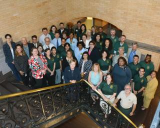 Photo of a large group posing together on the stairs of a large building.