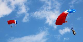 Two smokejumpers hanging from parachutes on final approach to land.