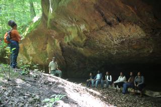 Students seated outdoors on a log under an overhang during a visit to Wayne National Forest.