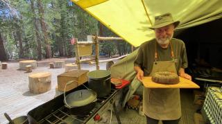 A person holding a cake he baked in the wilderness.