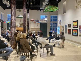 A group of people sitting in a galleria, listening to a speaker who sits infront of them.