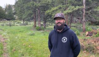 Dayton Cleveland with hands behind his back, standing in a thinned areas of a forest.