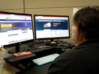 woman sits at desk using a computer with 2 screens