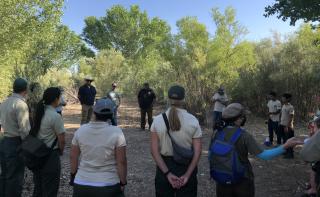 Tribal youth corps members and Forest Service employees stand in a circle in a clearing surrounded by trees.