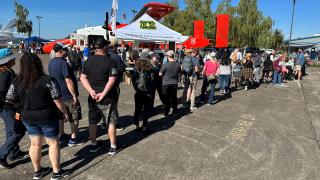 Long line of people waiting to tour Forest Service plane. Forest Service insignia on tent and plane are visible beyond the line.