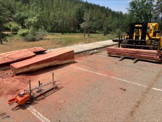 A parking lot, where chunks of a sequoia tree are piled on the left and a tractor is being used to moved others on the right