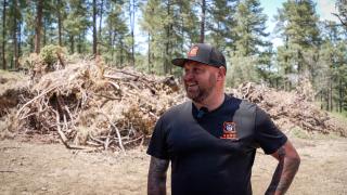 Sean Donaldson with a smile on his face, standing in front of a large brush pile in a forest.