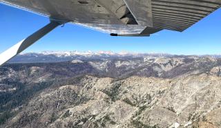 Mountains seen through an airplane window. The bottom of the right wing is also visible.