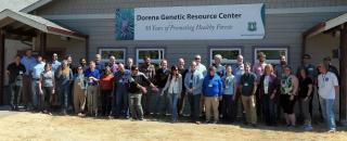 Large group of workshop attendees stands outside building under a sign. Sign has a picture of a pinecone and text: Dorena Genetic Resource Center; 50 years of promoting healthy forests. USDA Forest Service insignia is in lower right corner.