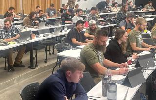 A large group of people sitting at tables and working intently on computers in front of them.