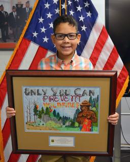 A kid holding a framed picture in front of him and smiling