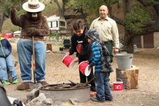 Image shows Smokey Bear supervising several children safely extinguish a campfire.