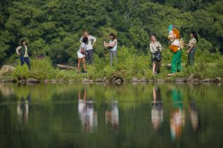 Image shows Woodsy Owl and several women picking up litter by a lake.
