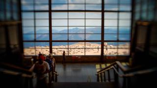 Image shows the inside of the Pikes Peak visitor center looking down stairs towards bay windows that show mountains beyond.