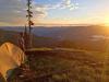 A picture of a camping tent setup up on a high mountain slope overlooking a beautiful sunset or sunrise.