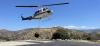 Helicopter just above pavement with water container dangling below.
