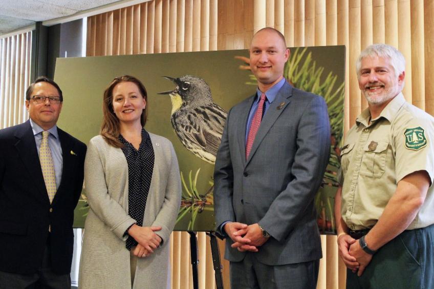 Three men and one woman standing in front of a photo of a bird