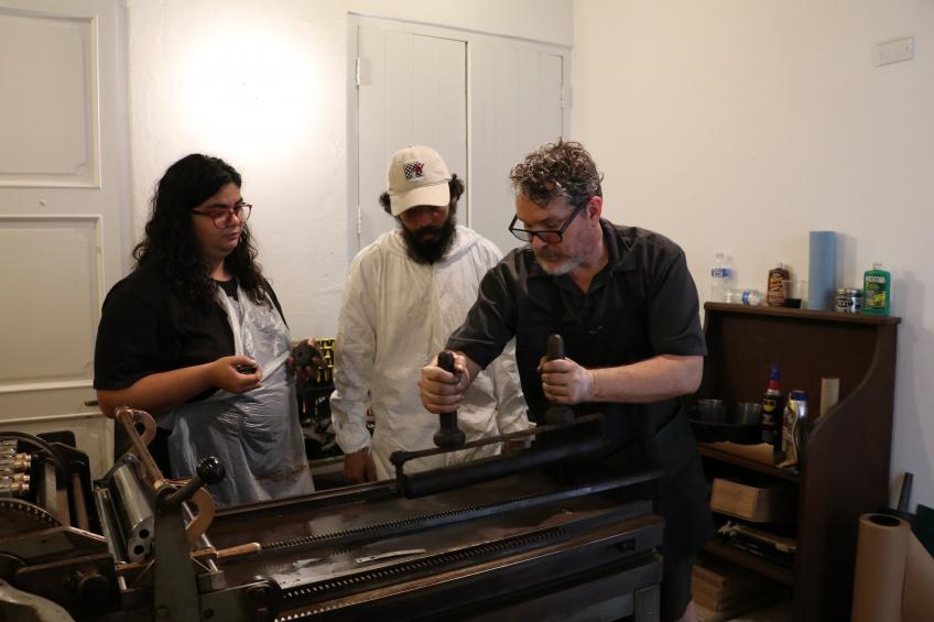 Man taching 2 students to use 19th century book press