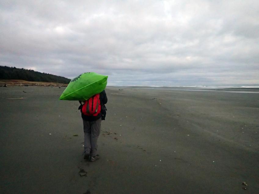 Russel Wicka walks along the beach in Alaska carrying a large bag of trash on his shoulder.