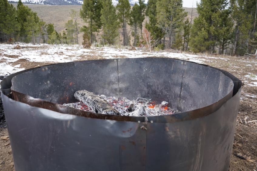 A double-walled pit burns down materials to produce biochar. Inside, woody material smolders.