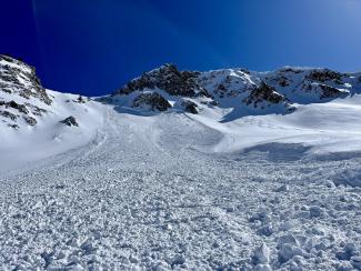 A large swath of snow from an avalanche with mountains in the back
