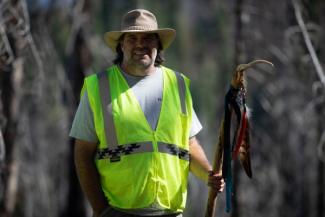 Man in bright yellow vest and hat carries walking stick with cross and feathers