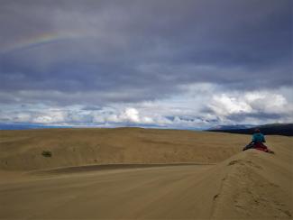 A woman sits on a barren landscape.