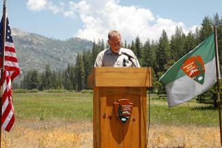 a male forest service employee speaking to a crown in a meadow behind a podium