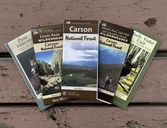 Five forest and wilderness maps displayed on a picnic table.