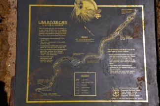 A metal plaque displays interpretive information about Lava River Cave in gold writing