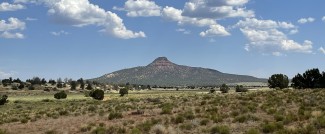 A lone rocky peak rises above a grassy plain beneath a partially cloudy sky.