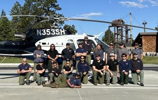 A group of firefighters pose in front of a firefighting helicopter.