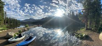 Two kayaks sit in lake with mountains and forest in background