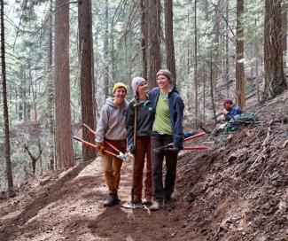 Three volunteers standing on a trail with tools posing with their arms around each other