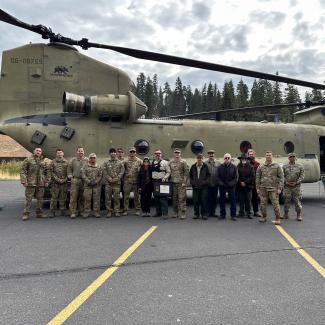 Soldiers and Forest Service employees stand in front of a helicopter and pose for a group photo