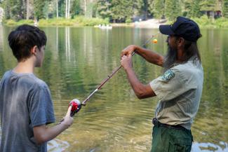 A forest service employee helps a kid fish.