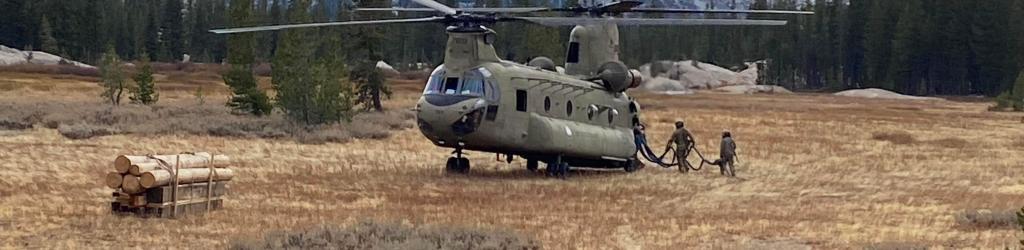 A helicopter is staged in the middle of a meadow with soldiers walking up to it and mountains in the background