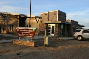 A photo of an office building, a sign in front of the building states, "Sioux Ranger District" "Camp Crook Fire Station".