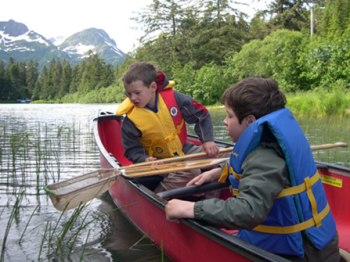 A photo of two boys in a paddle boat wearing life jackets.