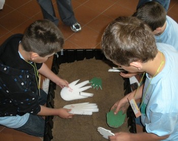 Kids sit over a box of sand with dinosaur foot models to create tracks.