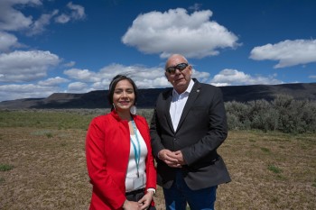 A man and woman pose standing next to each other in front of a sagebrush landscape and hills.